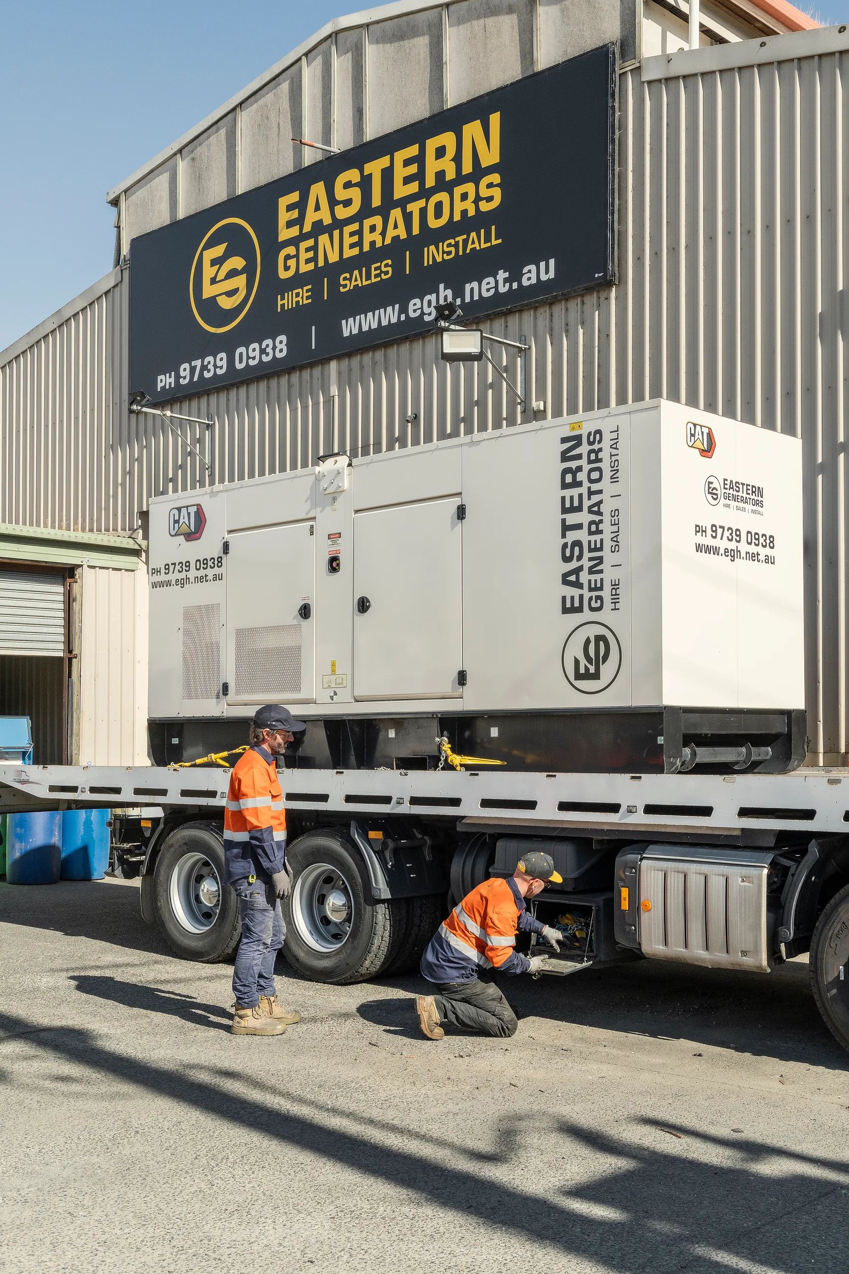 Crew alongside a large containerised generator loaded on a flatbed