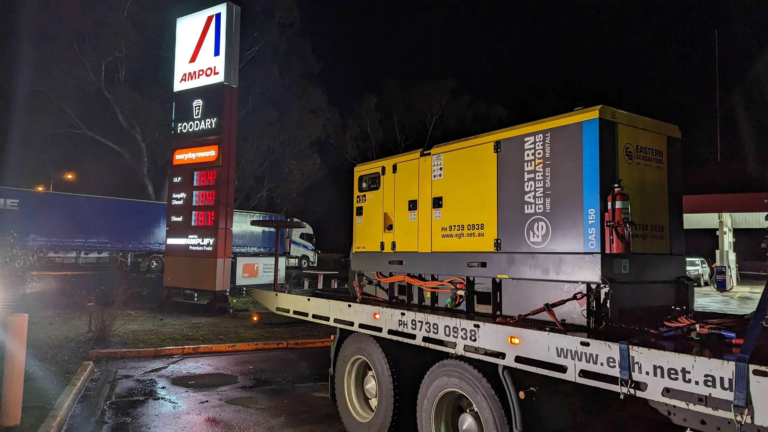 An Eastern Generators hire set secured on a flatbed at a service station at night